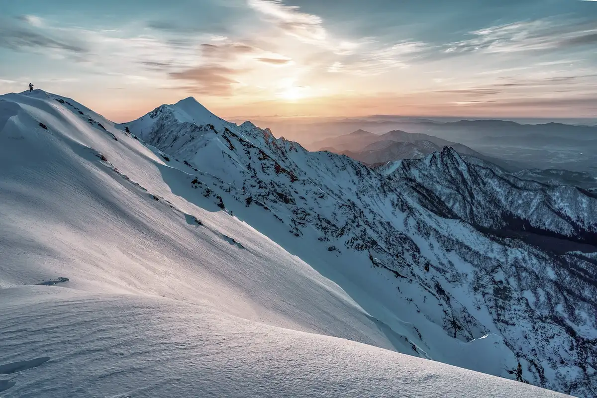 A snow covered ridge looking out over distant peaks at sunrise